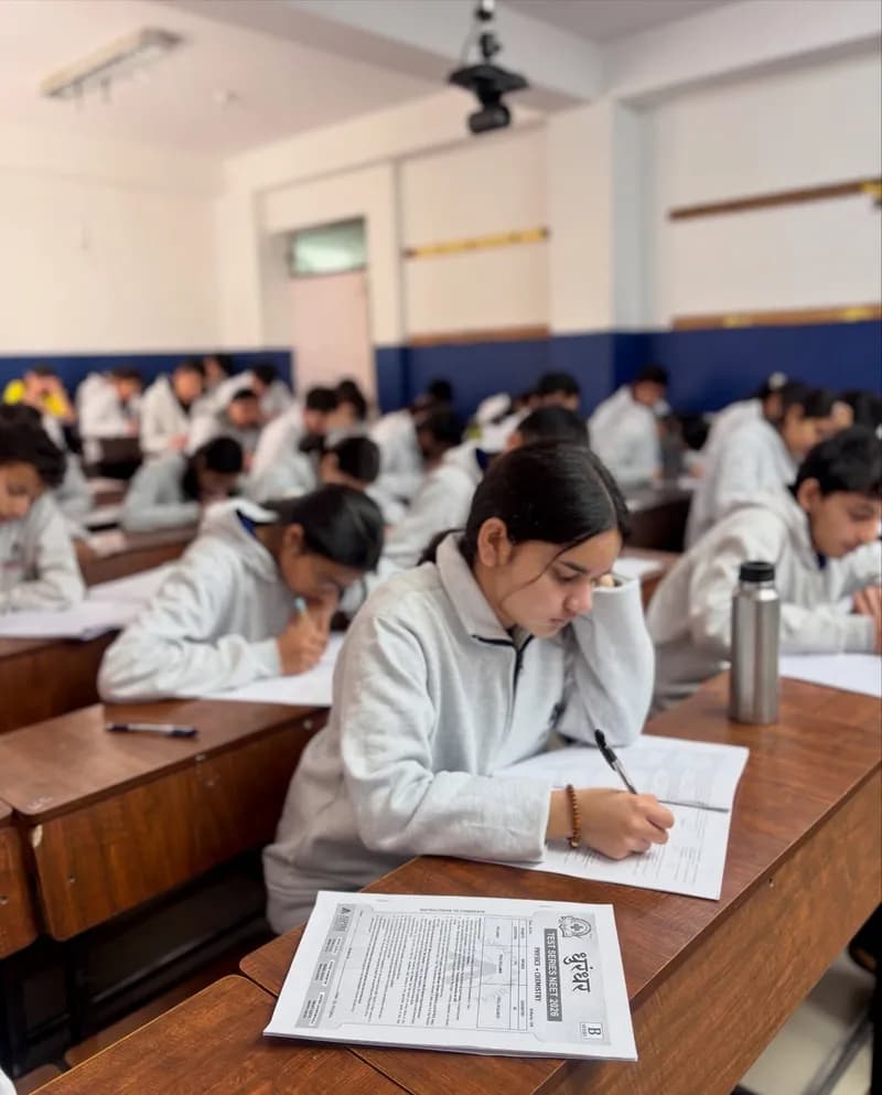 Students in grey Aspire hoodies writing a test at rows of desks in a bright classroom