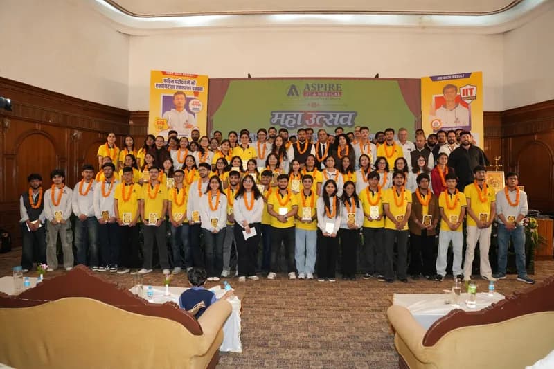 Large group of Aspire students in yellow and grey Aspire T-shirts and hoodies posing in a wood-panelled hall in front of a celebration banner