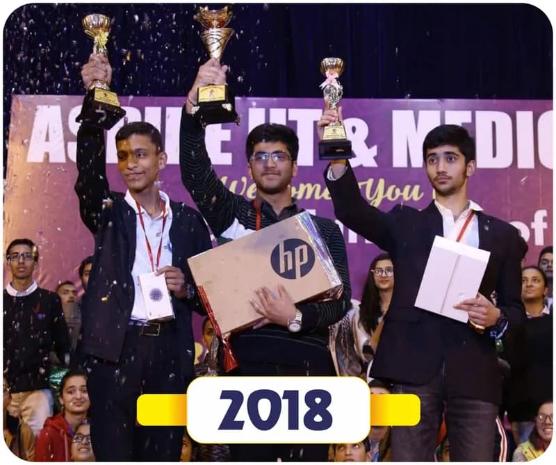 Brain of Himachal 2018: three winners in blazers holding up trophies and laptop prizes on stage (year label printed on the image)